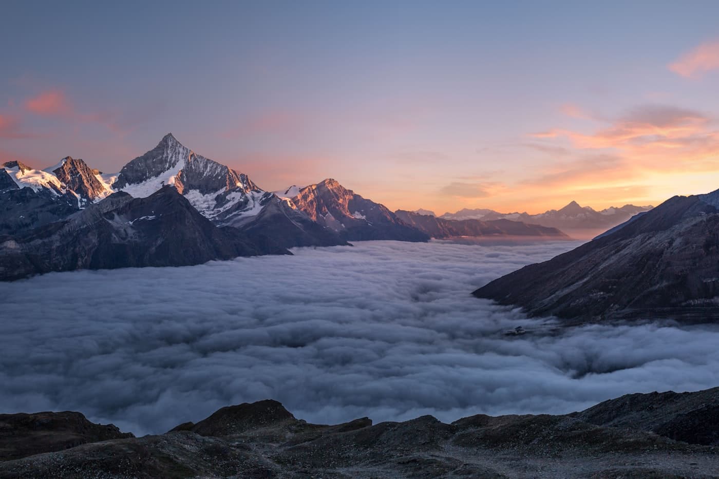 Snow-capped peaks rising above a sea of clouds at golden hour
