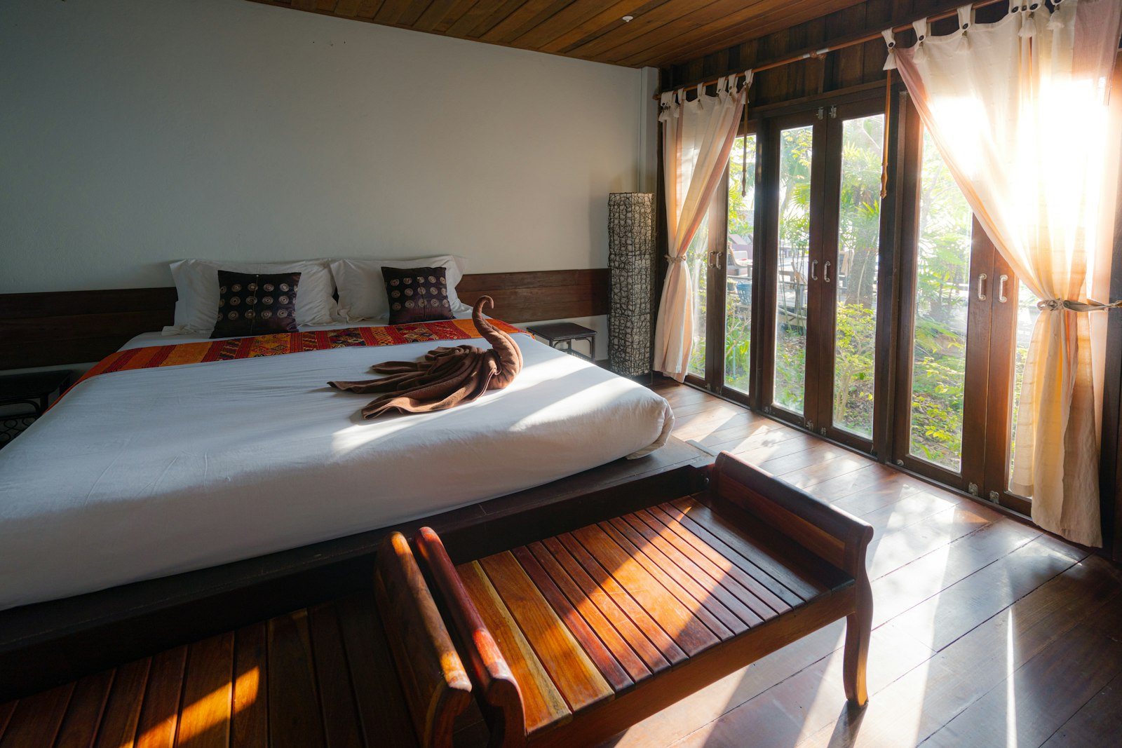 A sunlit luxury suite with linen-draped bed and a view toward the water